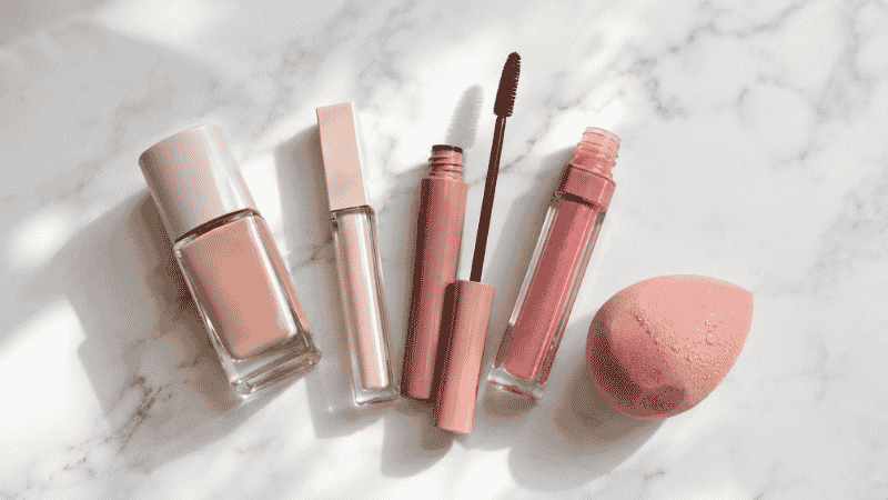 Beginner makeup products laid out on marble — foundation, concealer, mascara, and lip gloss