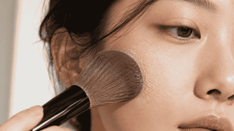Fluffy brush applying translucent setting powder before blush application
