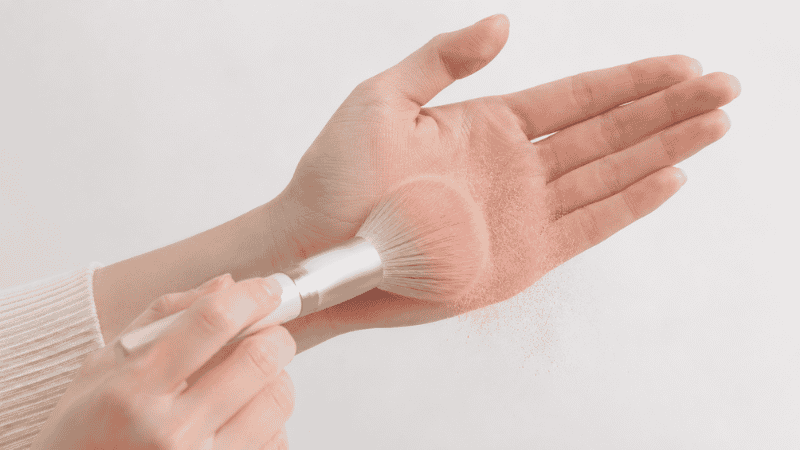 Tapping excess blush off a fluffy brush before applying to avoid over-application