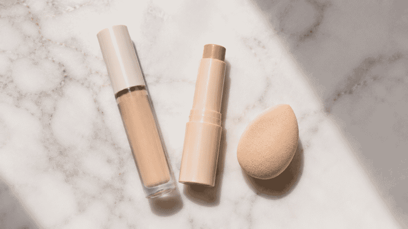 Concealer products and a beauty sponge arranged on a white surface for a beginner makeup tutorial