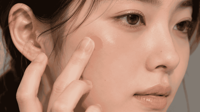 Fluffy brush applying powder blush to cheekbones in a sweeping upward motion