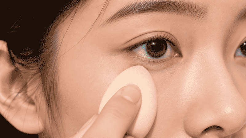Damp beauty sponge pressing concealer into skin for a seamless skin-like finish