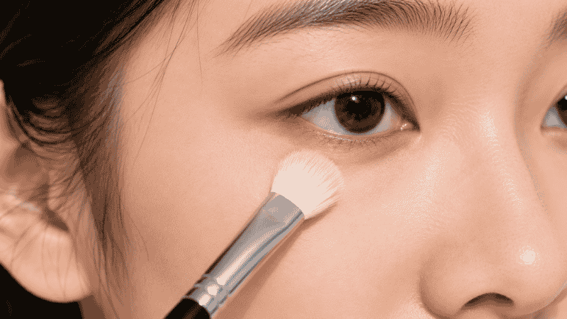 Fluffy brush dusting translucent setting powder under eyes to prevent concealer creasing