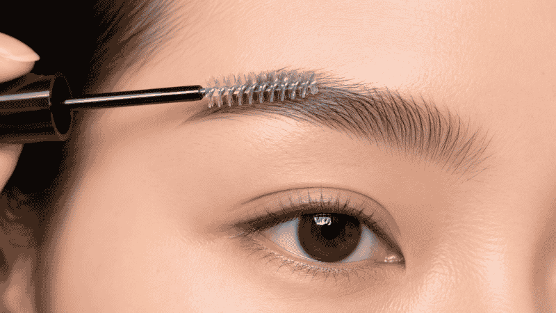 Clear brow gel being applied through eyebrows with a spoolie wand to set and hold hairs in place