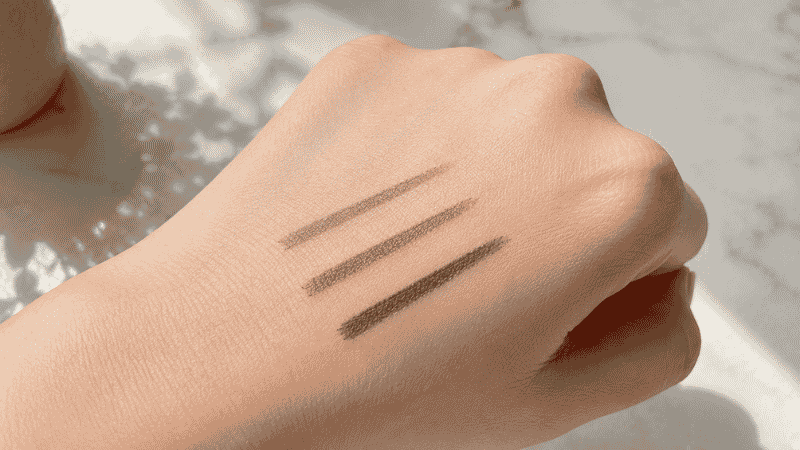 Three eyebrow pencils in different brown shades swatched on skin for shade comparison
