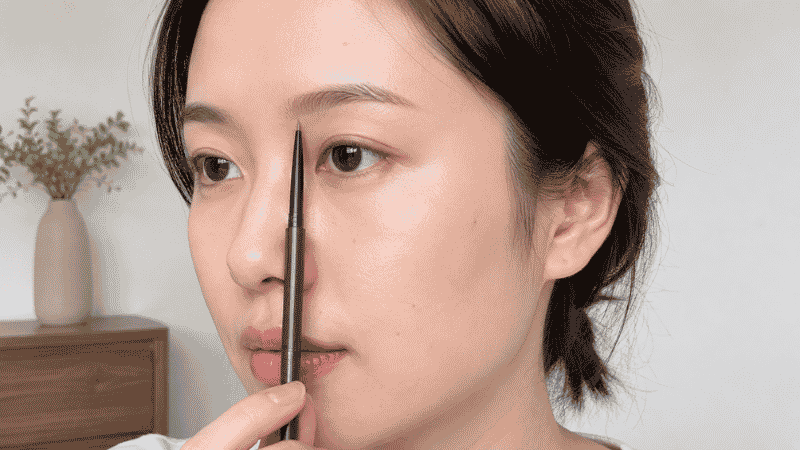 Straight pencil held vertically against nose to measure correct eyebrow start point using the 3-point rule