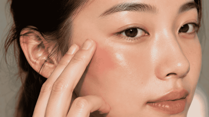 Cream blush applied high on the cheekbone sweeping toward the temple for the clean girl makeup aesthetic