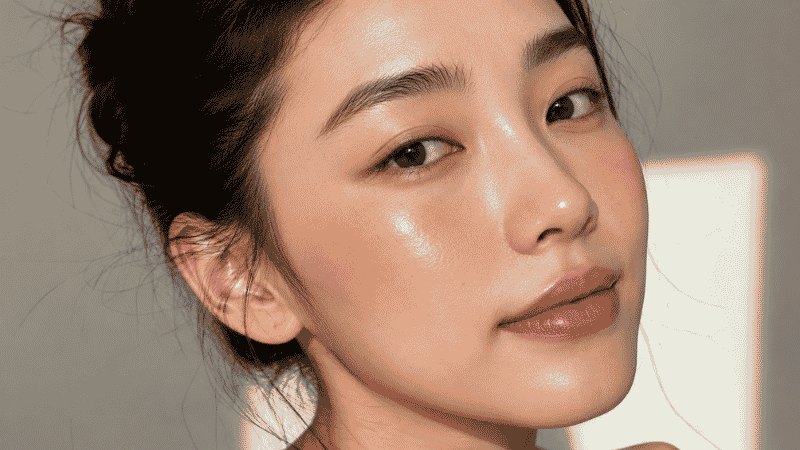 Woman with glowy dewy skin and minimal clean girl makeup including brushed brows high blush and glossy lips