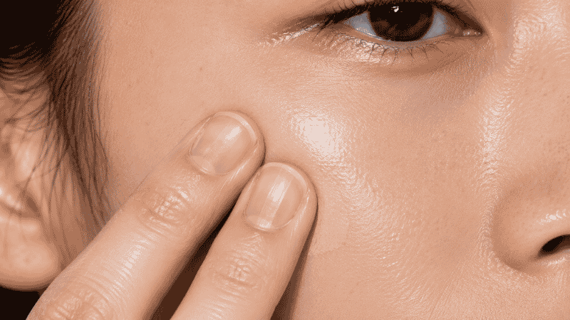 Fingers pressing a small amount of skin tint into cheek for a natural seamless skin-like finish