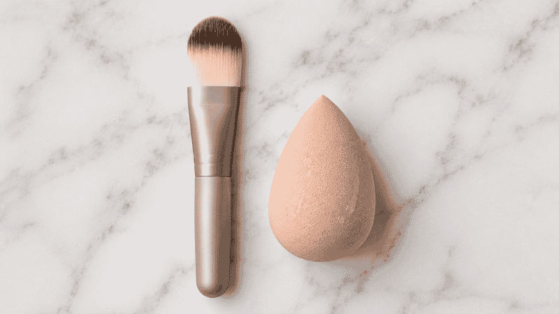 Foundation brush and damp beauty sponge placed side by side showing two different makeup application tools for comparison
