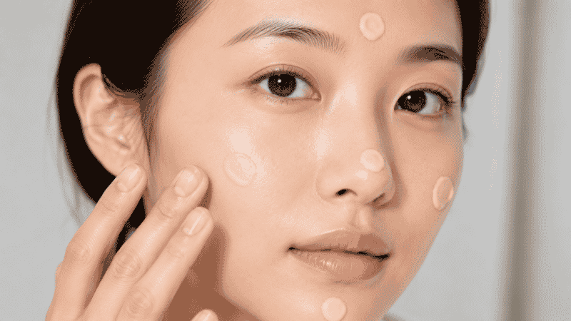 Tinted moisturizer being dotted onto face at five points then blended with fingertips in a pressing motion