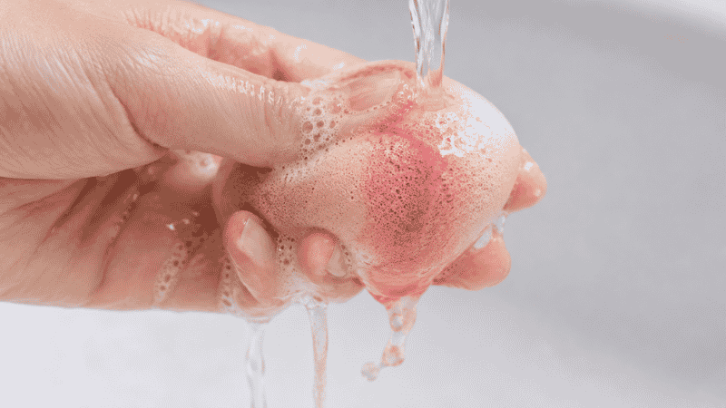 Damp beauty sponge being squeezed with cleanser showing pink makeup residue releasing during cleaning process