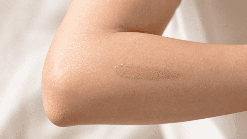 Small amount of foundation being applied to the inside of an arm near the elbow to patch test for skin reactions
