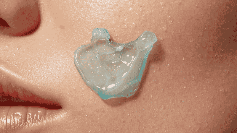 A macro texture shot of a translucent blue water-gel moisturizer being applied to skin, showing its weightless and non-greasy consistency.