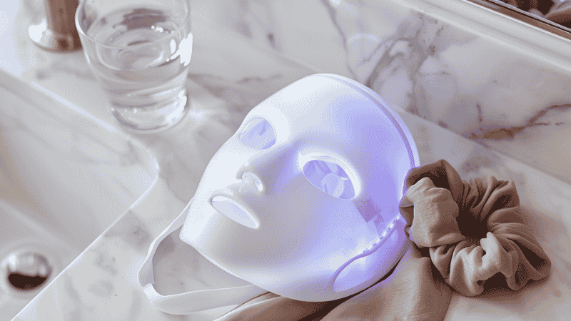 A professional-grade Qure LED light therapy mask placed on a minimalist white marble bathroom vanity, symbolizing a simplified 3-minute skincare routine